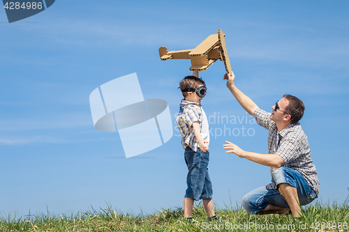 Image of Father and son playing with cardboard toy airplane in the park a