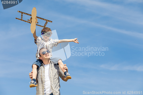 Image of Father and son playing with cardboard toy airplane in the park a