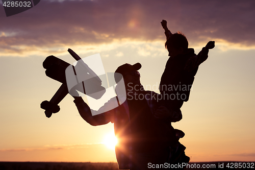 Image of Father and son playing with cardboard toy airplane in the park a