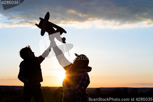 Image of Father and son playing with cardboard toy airplane in the park a