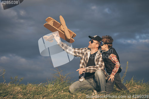 Image of Father and son playing with cardboard toy airplane in the park a