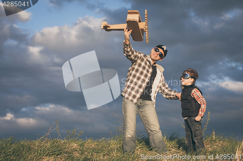 Image of Father and son playing with cardboard toy airplane in the park a