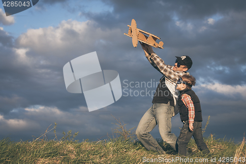 Image of Father and son playing with cardboard toy airplane in the park a