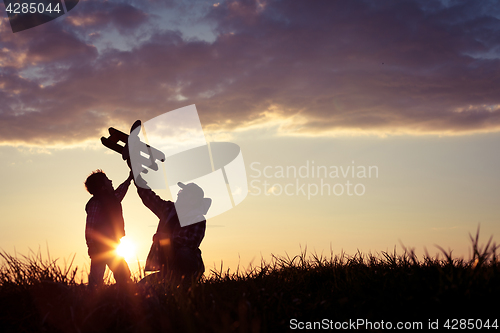 Image of Father and son playing with cardboard toy airplane in the park a