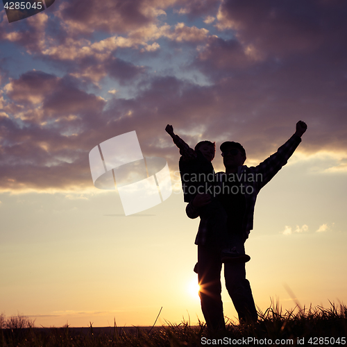 Image of Father and son walking on the field at the sunset time.