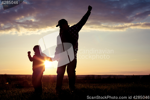 Image of Father and son walking on the field at the sunset time.