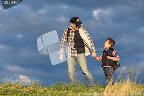 Image of Father and son walking on the road at the day time.