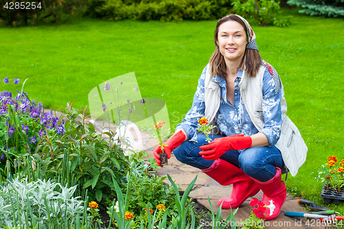 Image of smiling woman in kerchief and red boots planting flowers