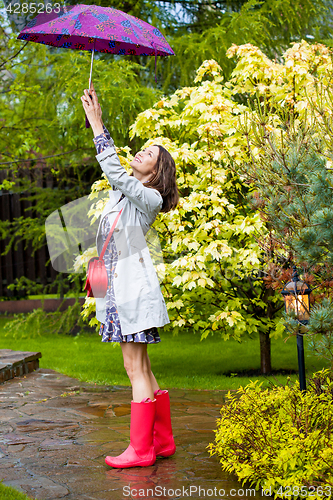 Image of Beautiful smiling woman in red rubber boots and with an umbrella