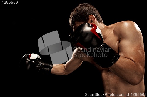 Image of Male boxer boxing in punching bag with dramatic edgy lighting in a dark studio