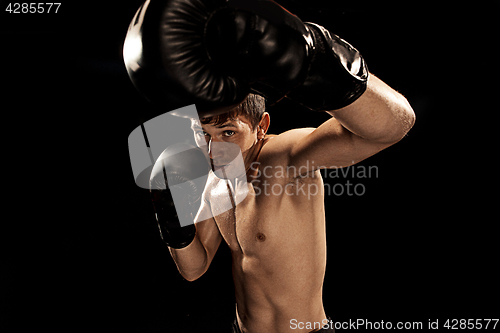 Image of Male boxer boxing in punching bag with dramatic edgy lighting in a dark studio