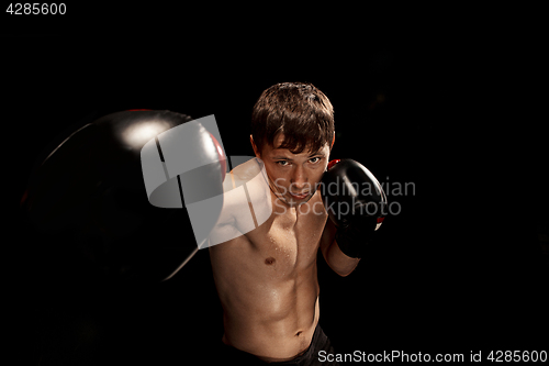 Image of Male boxer boxing in punching bag with dramatic edgy lighting in a dark studio