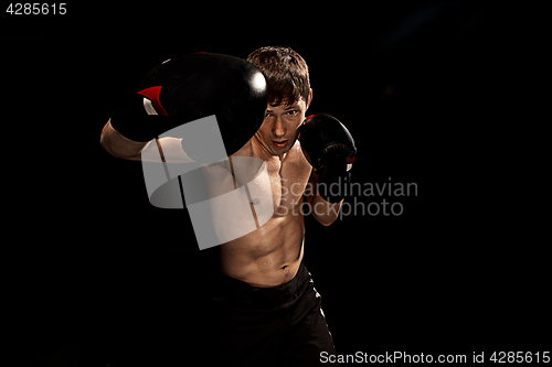 Image of Male boxer boxing in punching bag with dramatic edgy lighting in a dark studio