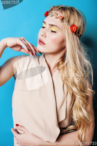 Image of young pretty blond girl with curly blond hair and little lowers happy smiling on blue sky background, lifestyle people concept