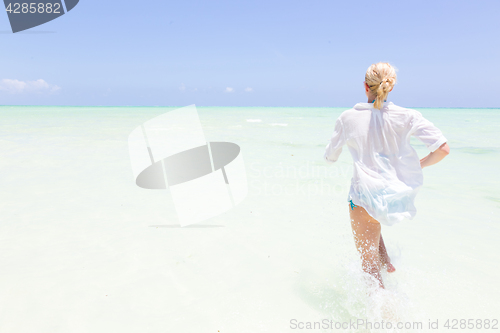 Image of Young active woman having fun running and splashing in shellow sea water.