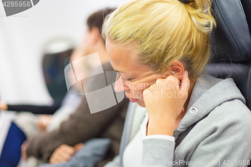 Image of Tired blonde woman napping on seat while traveling by airplane.