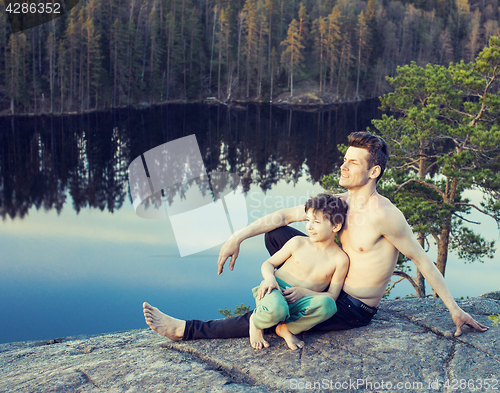 Image of middle age man with little cute son doing sport yoga on the top of the mountain together, happy family lifestyle people outdoor, summer wild nature for training 