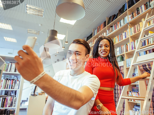 Image of couple students in univercity library, looking book, preparing to exam, having fun, making selfie, lifestyle people concept