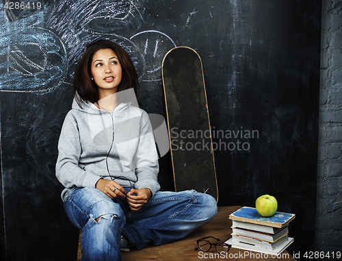 Image of young cute teenage girl in classroom at blackboard seating on table smiling, modern hipster concept, lifestyle people