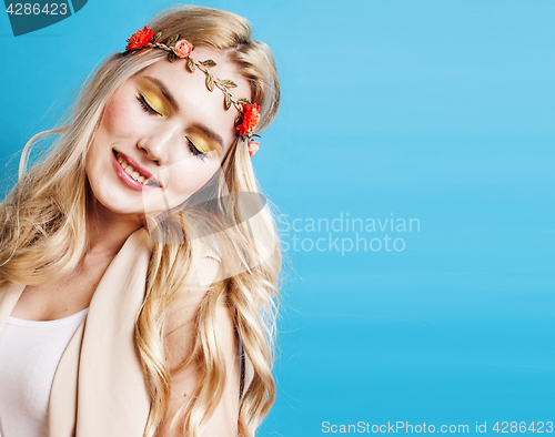 Image of young pretty blond girl with curly blond hair and little lowers happy smiling on blue sky background, lifestyle people concept 