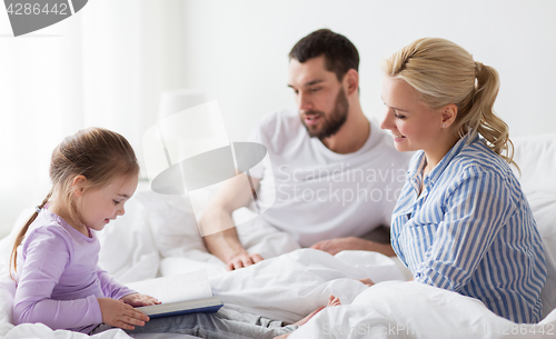 Image of happy family reading book in bed at home