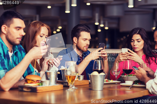 Image of friends with smartphones dining at restaurant