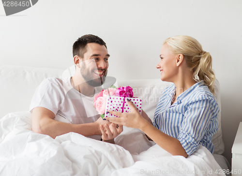 Image of happy couple with gift box in bed at home
