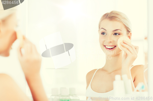 Image of young woman washing face with sponge at bathroom