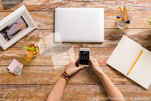 Image of hands with smartphone and laptop at office table
