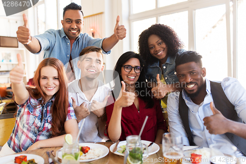 Image of happy friends showing thumbs up at restaurant
