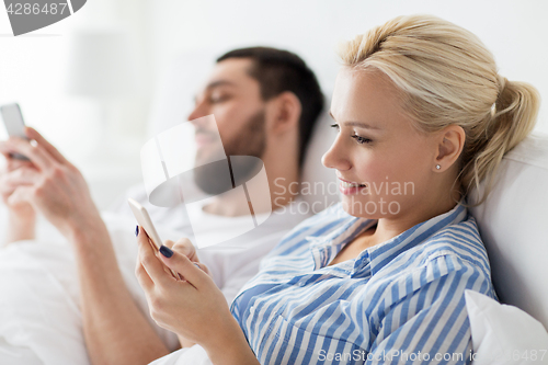 Image of couple with smartphones in bed at home