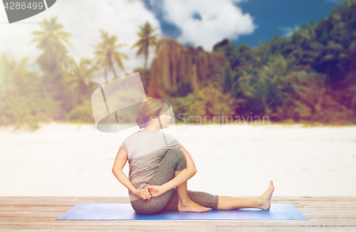 Image of woman doing yoga in twist pose on beach