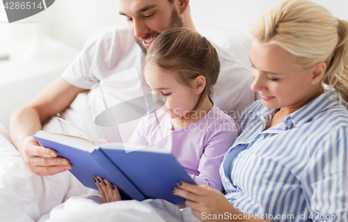 Image of happy family reading book in bed at home