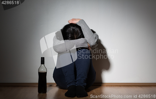Image of woman with bottle of alcohol crying at home