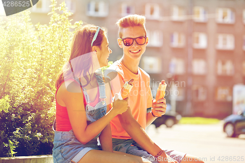 Image of happy teenage couple eating hot dogs in city