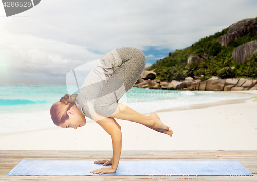 Image of woman doing yoga in crane pose on beach