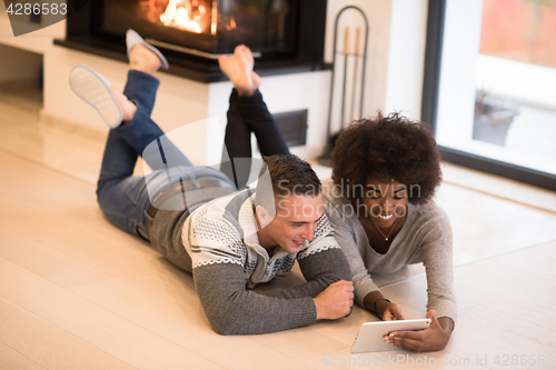 Image of multiethnic couple using tablet computer on the floor