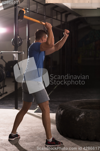 Image of man workout with hammer and tractor tire