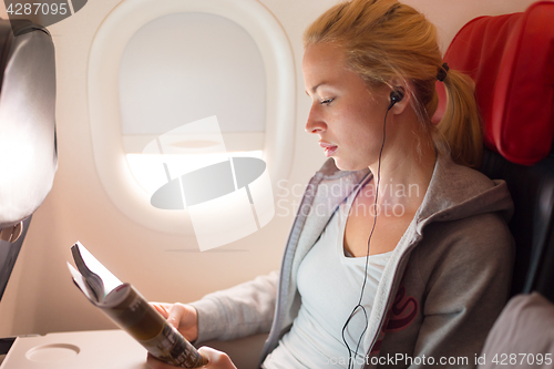 Image of Woman reading magazine and listening to music on airplane.