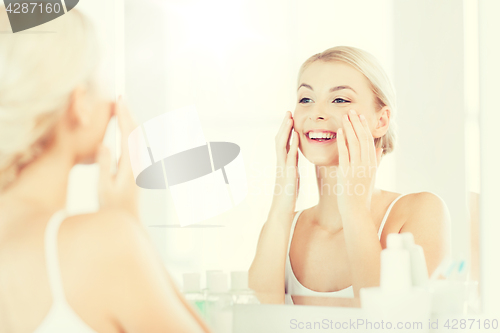 Image of happy woman applying cream to face at bathroom