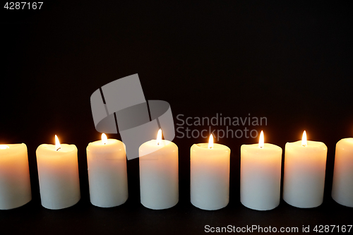 Image of candles burning in darkness over black background