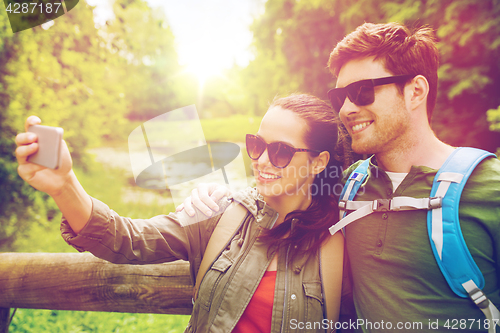 Image of couple with backpacks taking selfie by smartphone