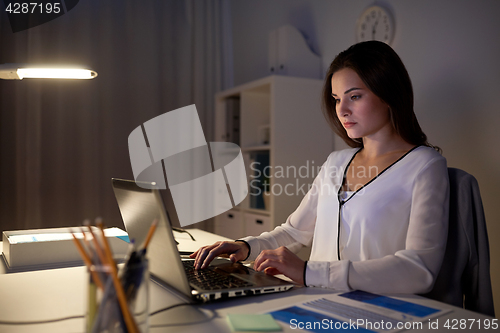 Image of businesswoman with laptop at night office