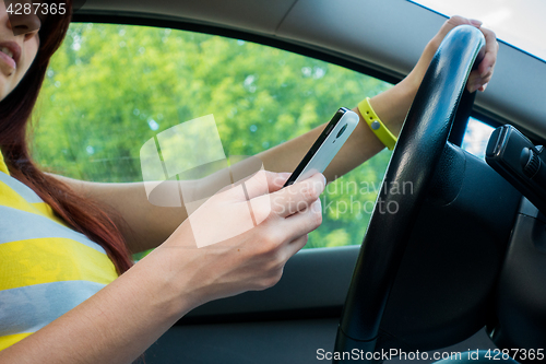 Image of Woman driver sitting behind the steering wheel reading a text message on a mobile