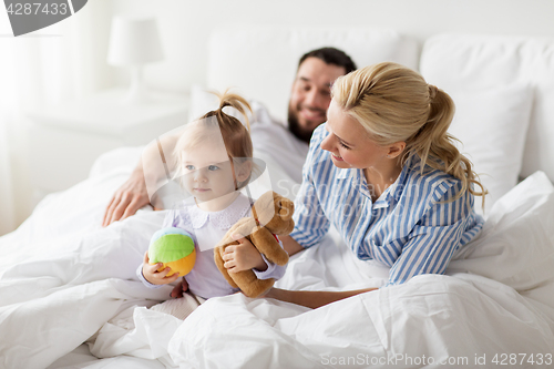 Image of happy child with toys and parents in bed at home