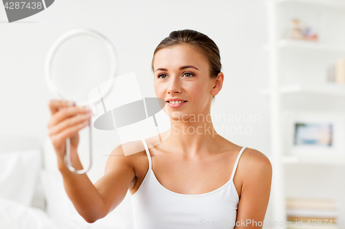 Image of beautiful woman with mirror sitting on bed at home