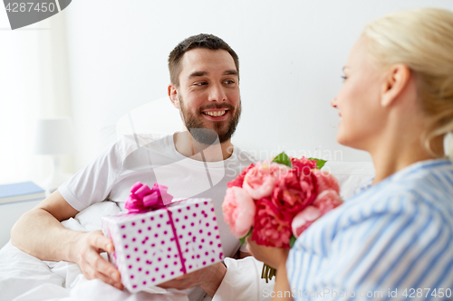 Image of happy couple with gift box in bed at home