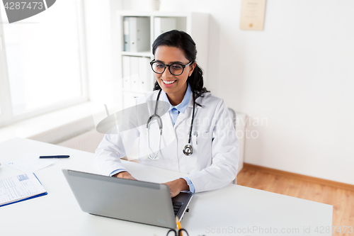 Image of happy female doctor typing on laptop at hospital