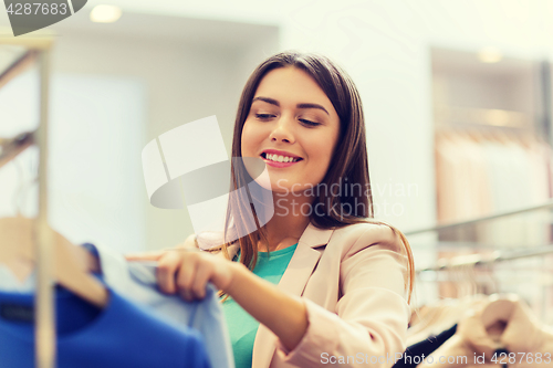 Image of happy young woman choosing clothes in mall