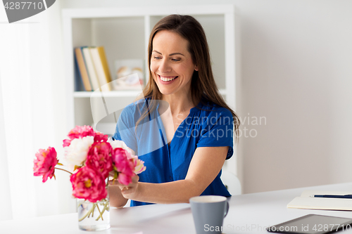 Image of woman setting flowers in vase on office table